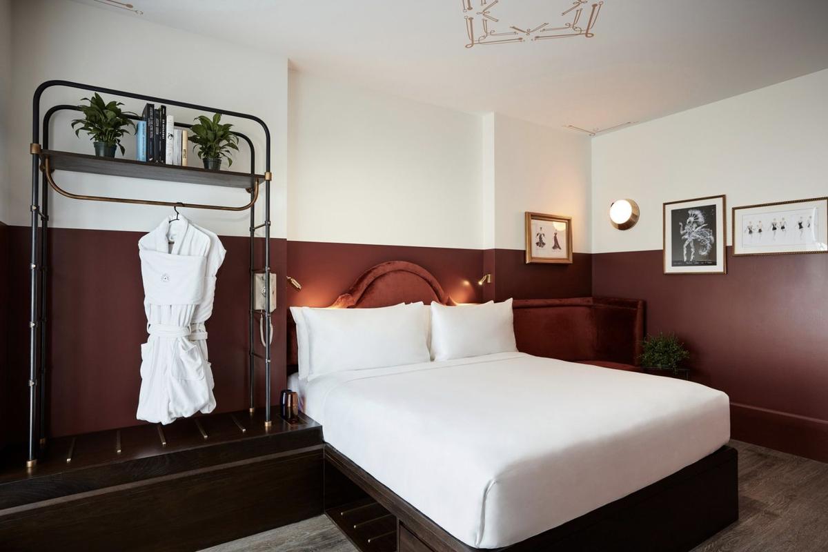 A Spacious King room: a king bed, burgundy and white walls, framed art and an open rack with a robe